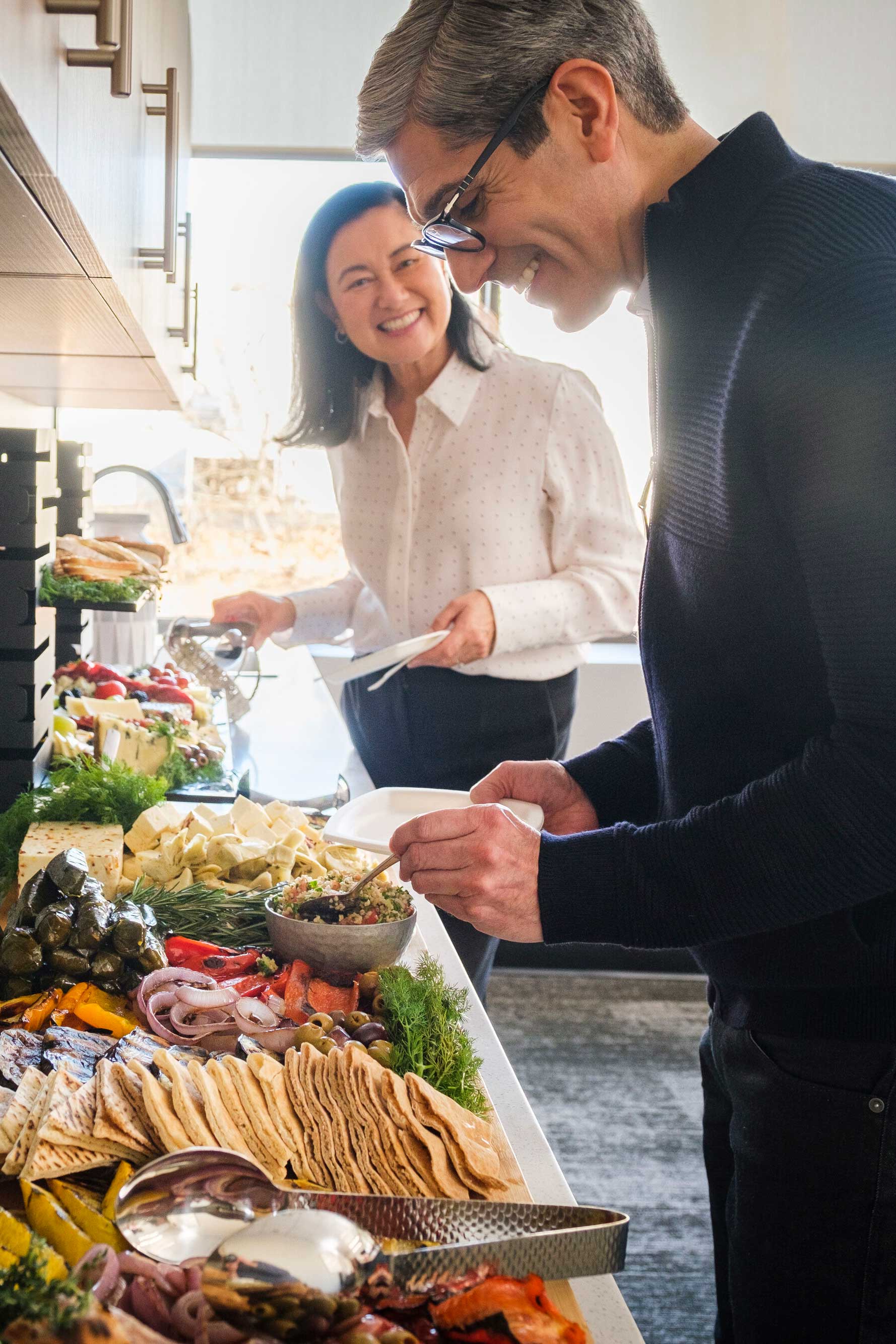 Two people grabbing food from catered buffet